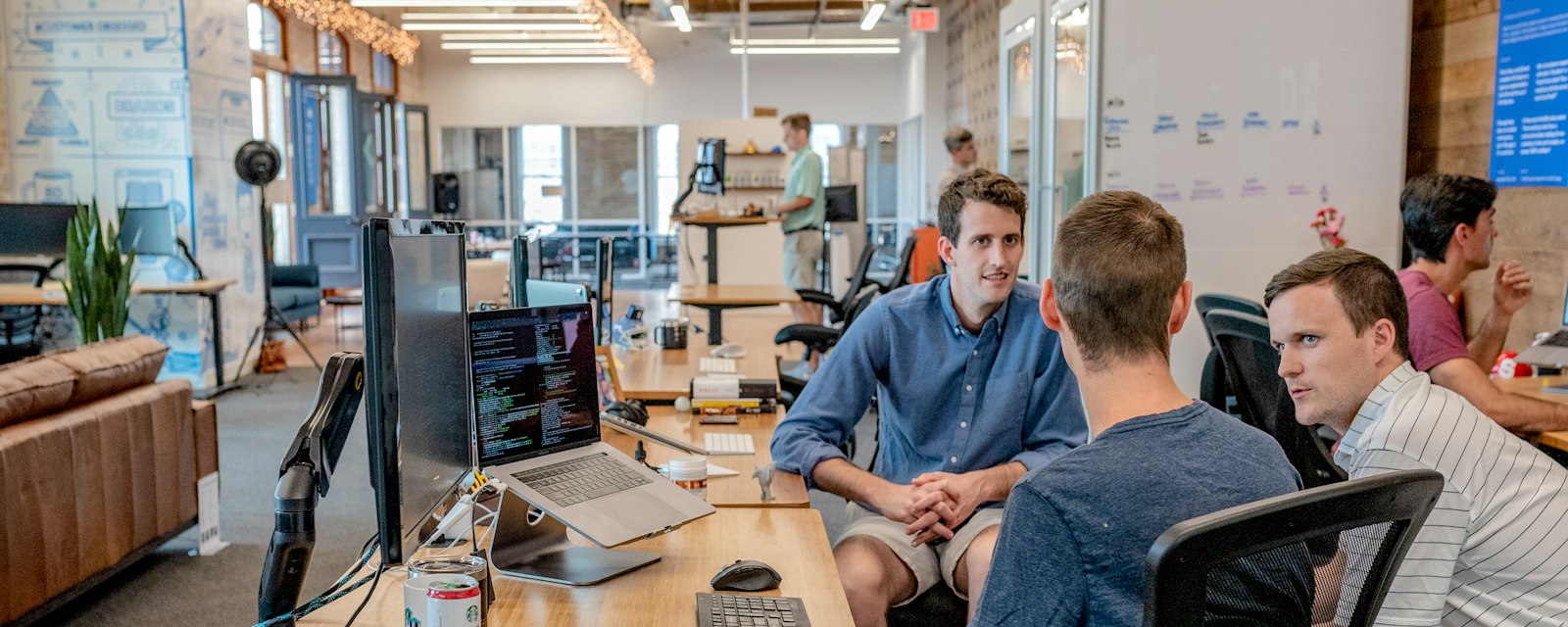 A team meeting around a table in a modern office, with charts on a whiteboard behind them